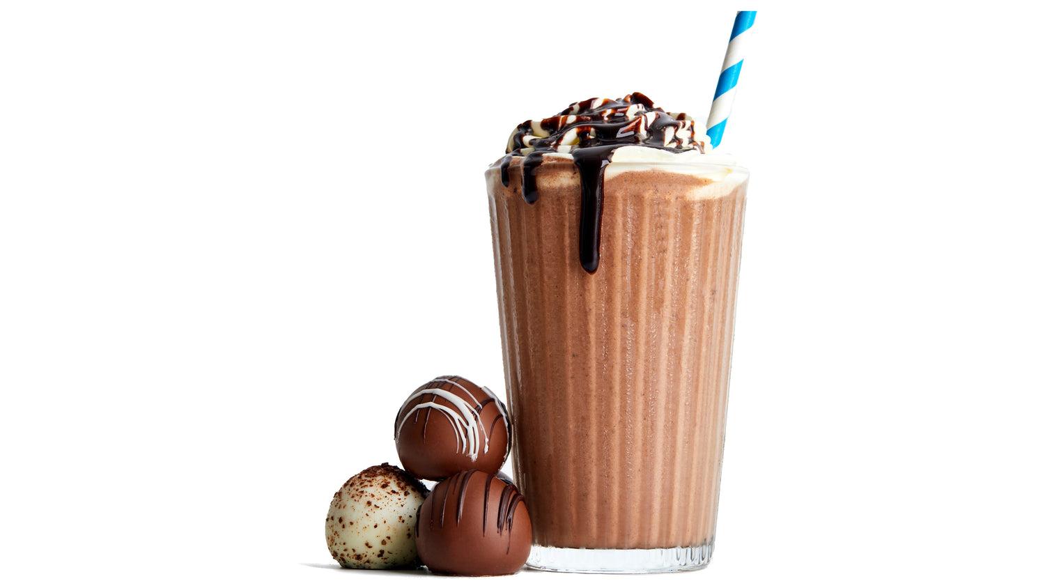 A glass of chocolate milkshake topped with whipped cream and chocolate syrup, with a blue-and-white striped straw, next to three assorted chocolate truffles, on a white background.